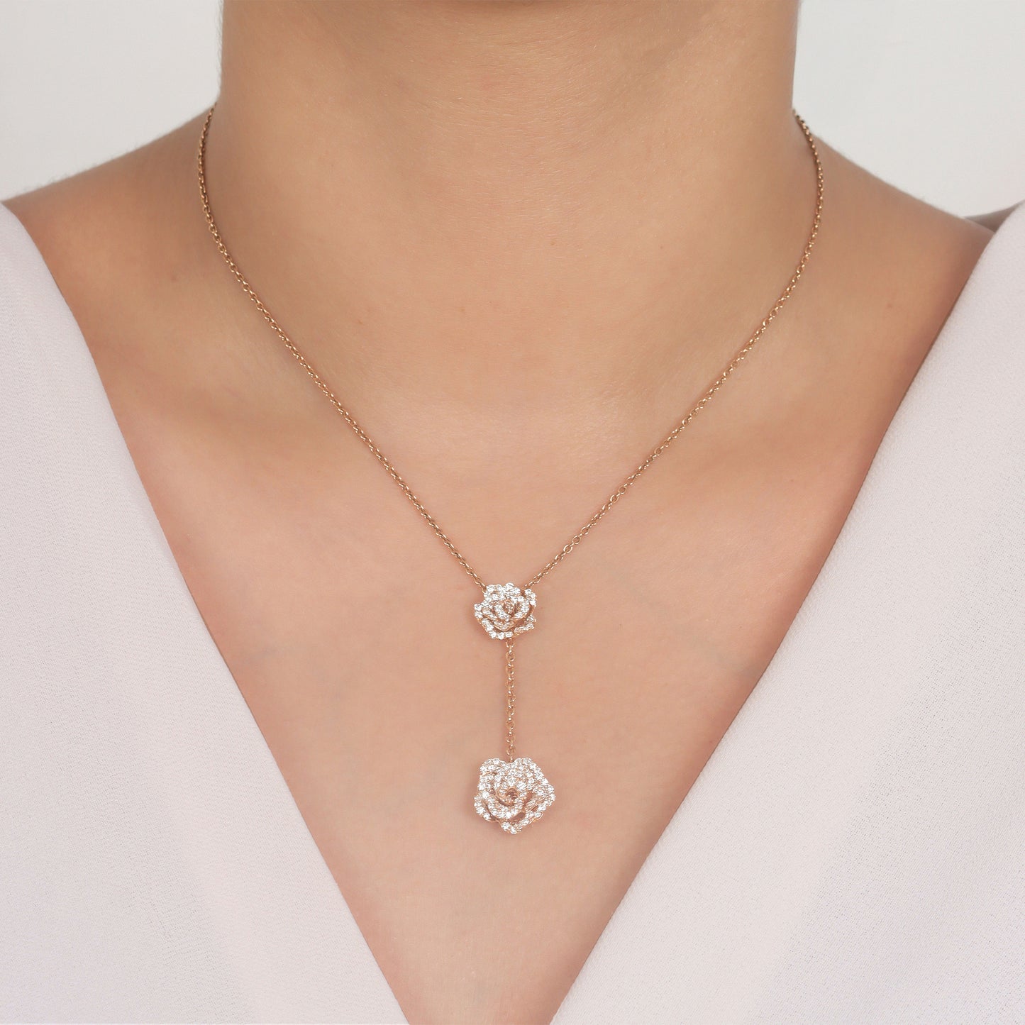 Rose gold necklace with floral pendants on a person wearing a white top.