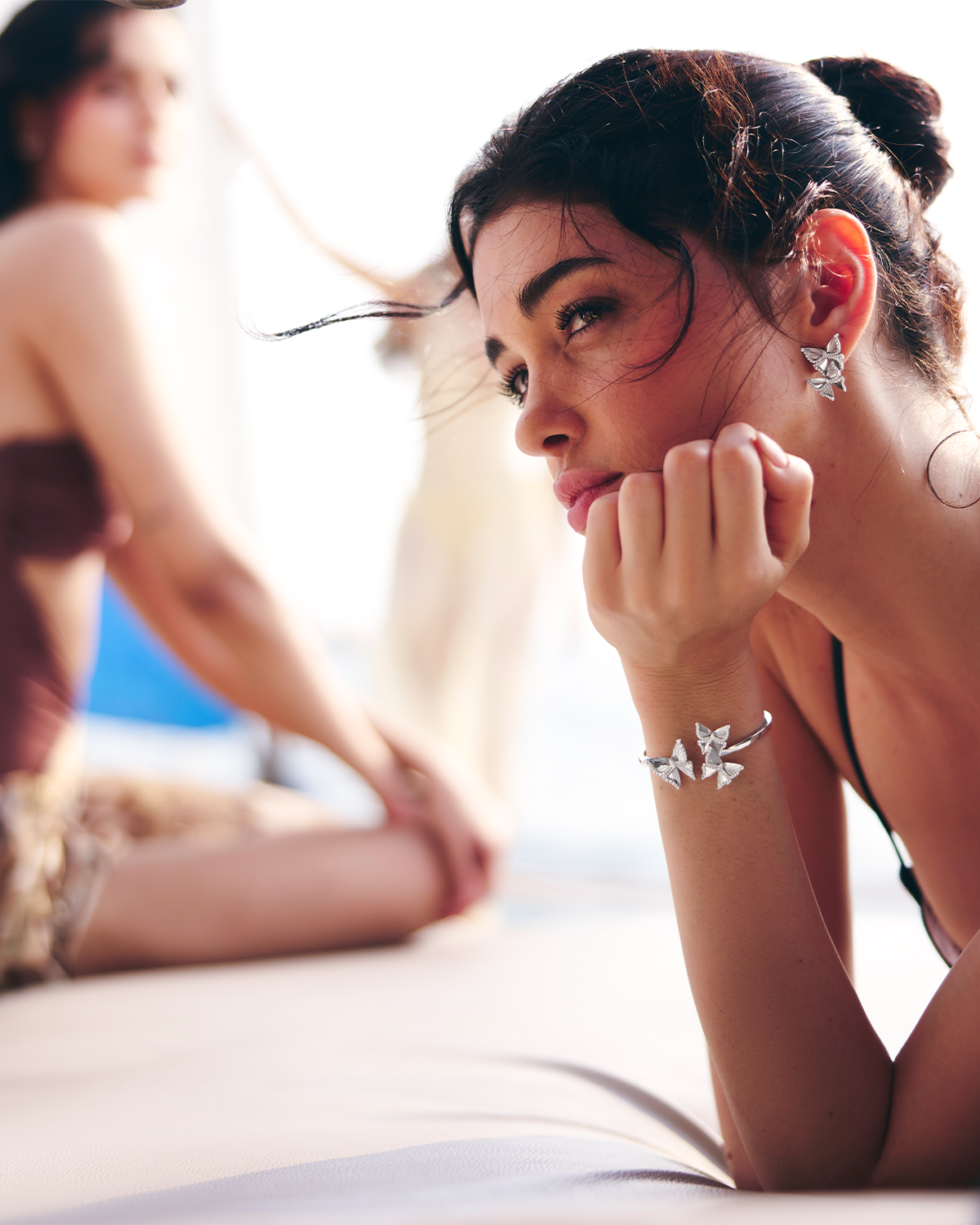 Woman wearing butterfly earrings and a bracelet, with another person in the background.