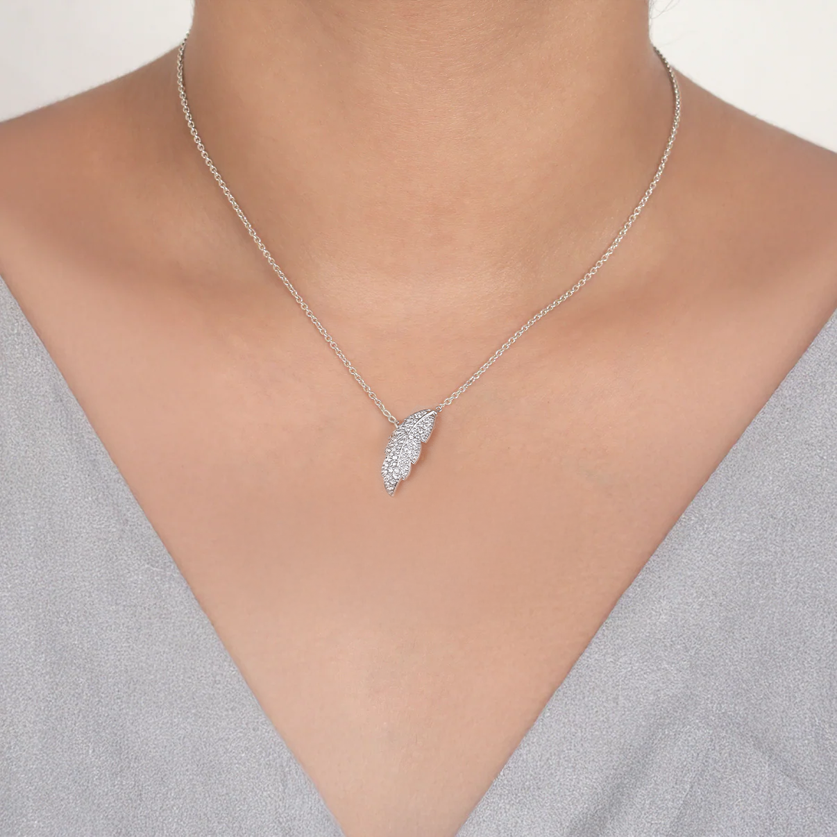 Silver necklace with a leaf-shaped pendant on a model wearing a gray top.