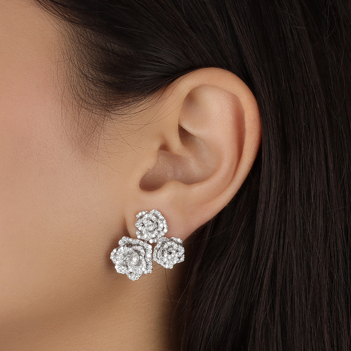Close-up of an ear wearing a pair of floral diamond earrings with dark hair and skin background.